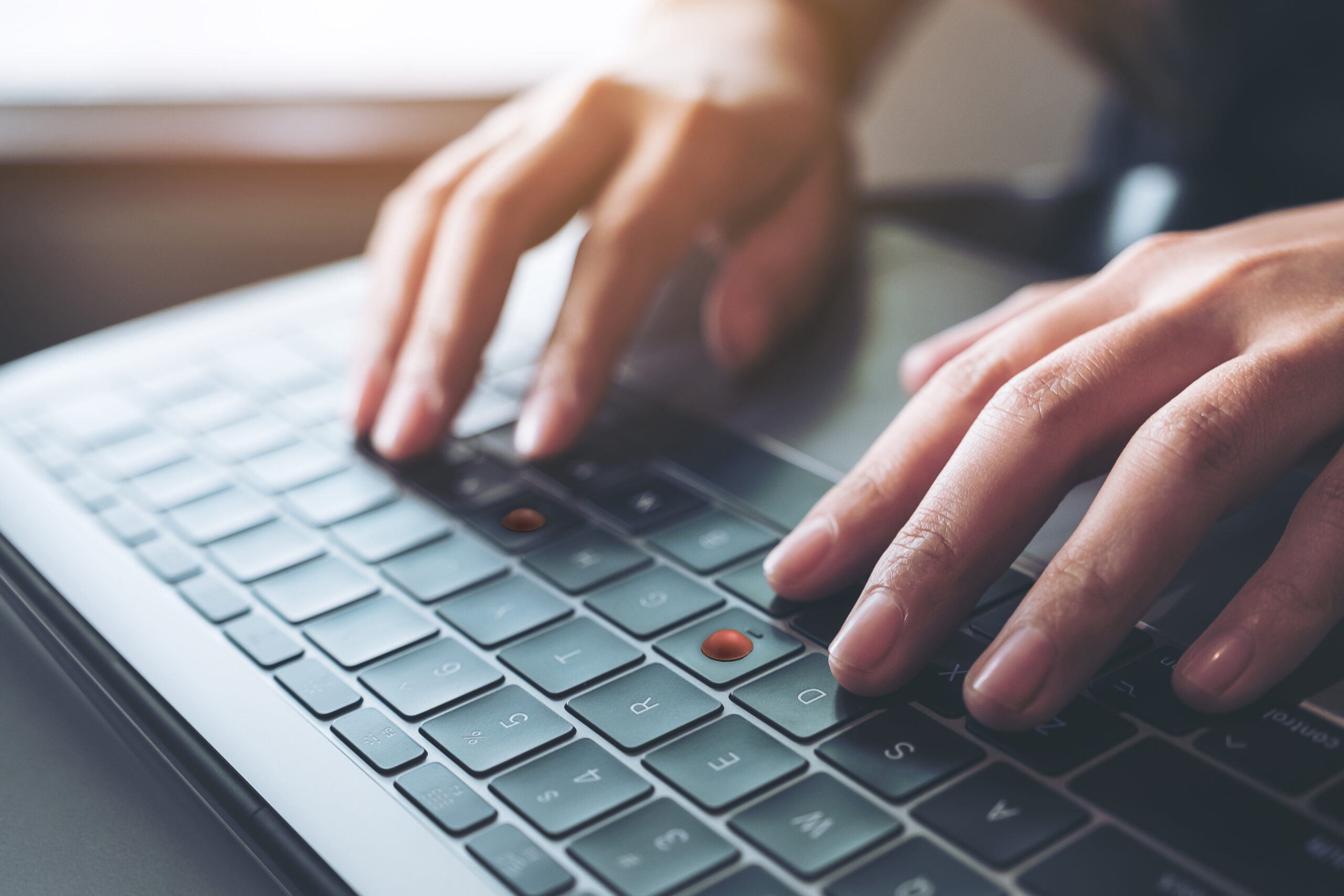 Close-up of hands typing on a laptop keyboard with raised tactile dots on some keys for finger placement identification.