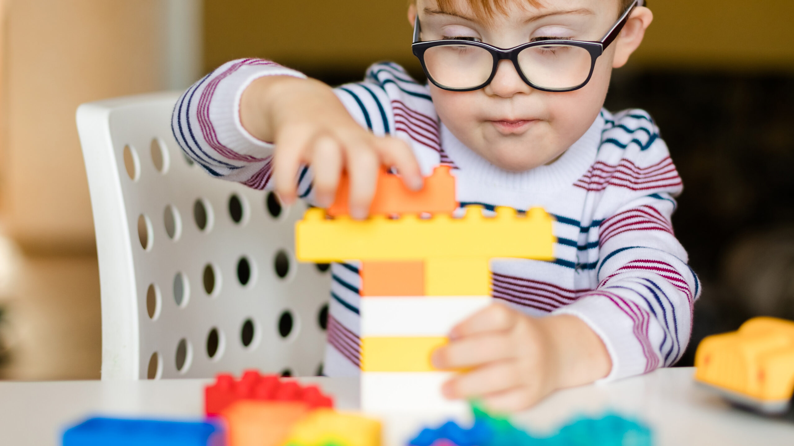 Young child wearing glasses stacks colorful building blocks during a learning activity